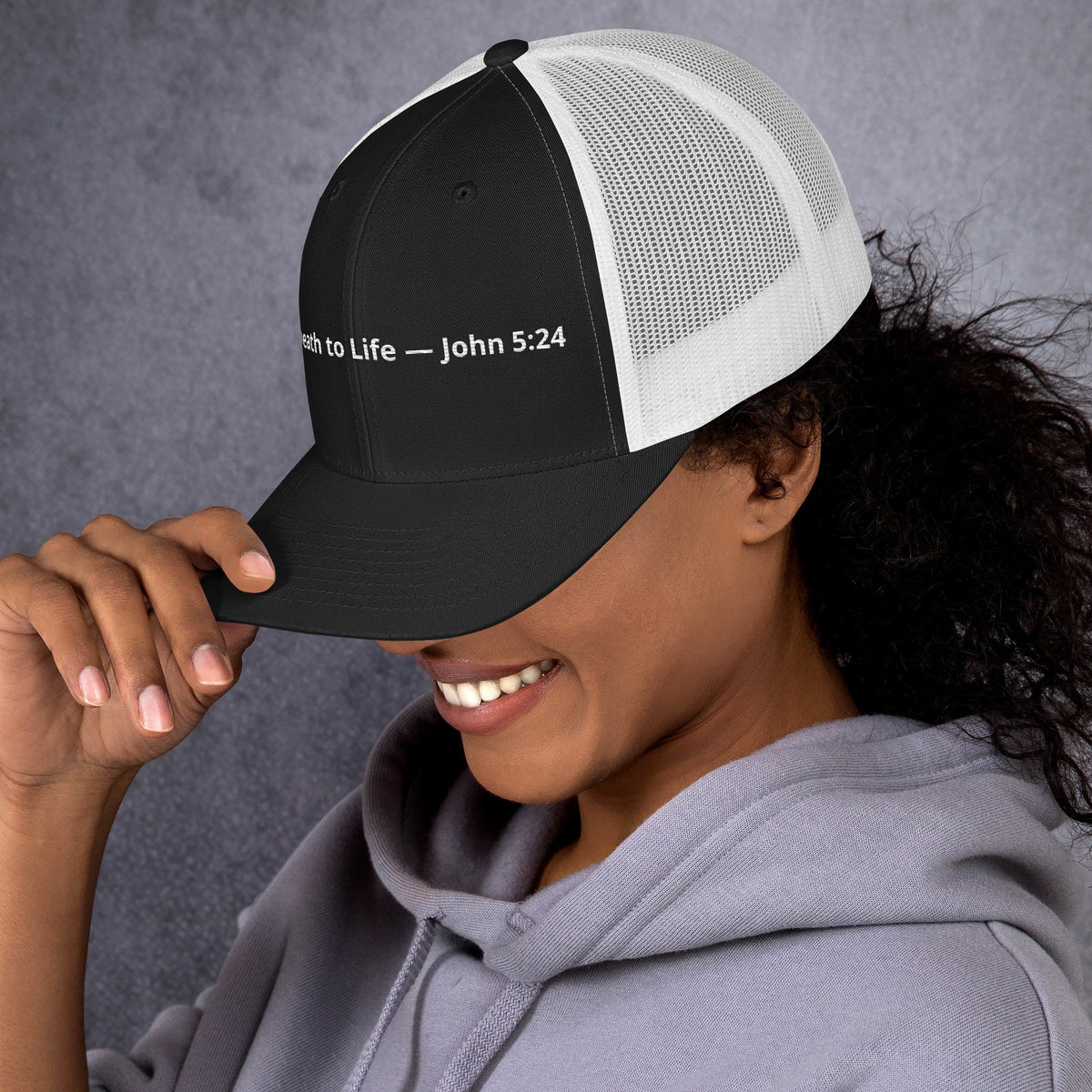 Black and white retro trucker hat featuring Christian message from John 5:24, styled with a classic mesh back and curved brim.